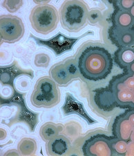 Figure 1: A closeup crop of complex chalcedony spherulites from an Ocean Jasper specimen, similar to that of Fig. 1 in Lieber. Archetypes in this specimen: 'flower-burst' spherulites, or spherically-banded spherulites with pseudomorphic crystalline quartz growth as outer 'petals'; agate-type banding; quartz druzy pockets with botryoidal chalcedony growth; flow of particulates that are likely of iron mineral content, found in many specimens from both Marovato and Kabamby. Note Lieber questioned whether these particulates were 'lepidocrocite', an iron-hydroxide mineral that is commonly found in the weathering of primary iron minerals and in iron ore deposits. I have identified another possibility for the particulate flow, which is iron-oxide and hydroxide mineral precipitates from ferrous-silica solutions. This is consistent with the theory of formation that I have presented in my published book on Ocean Jasper. Note also that this specimen, like Lieber's, has the well-defined larger spherulite type that has been more commonly associated with later mined deposits, between 2005-2006. Picture height, ~40mm.