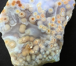 Figure 5 (Middle): Four different specimens showing spherulites 'swimming' in translucent chalcedony. The first three with clear chalcedony are likely from later collection finds, e.g. the two Marovato deposits ('veins 3/4') of 2013/14. The fourth (two closeups) with green chalcedony is from the earliest collection of translucent material, 1999/2000, and exhibits multiple ringed spherulites with vividly colorful nuclei that by eye show a random mixture of mineral particulates, e.g. iron oxide/hydroxide. Lieber's specimen in his Fig. 5 (Middle) is a quite rare green translucent with small (mm, sub-mm) round white/cream spherulites, and is a small closeup (10mm width). The colorful specimen shown here has much larger compound spherulites (5mm average). Translucent specimens with spherulites were reportedly found in early mined deposits, though due to the lack of cataloguing and documentation, we are largely unaware of just what types of translucents were mined, when and where. The colorful types span deposits 1-4 and are often smoothly 'connected' to, or interconnected with, semi-translucent or opaque varieties. I show an example of this in the Photo Gallery 16, and there are several examples in my book. Picture/specimen height: ~35mm.