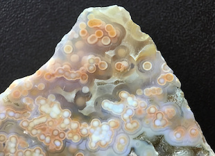 Figure 5 (Middle): Four different specimens showing spherulites 'swimming' in translucent chalcedony. The first three with clear chalcedony are likely from later collection finds, e.g. the two Marovato deposits ('veins 3/4') of 2013/14. The fourth (two closeups) with green chalcedony is from the earliest collection of translucent material, 1999/2000, and exhibits multiple ringed spherulites with vividly colorful nuclei that by eye show a random mixture of mineral particulates, e.g. iron oxide/hydroxide. Lieber's specimen in his Fig. 5 (Middle) is a quite rare green translucent with small (mm, sub-mm) round white/cream spherulites, and is a small closeup (10mm width). The colorful specimen shown here has much larger compound spherulites (5mm average). Translucent specimens with spherulites were reportedly found in early mined deposits, though due to the lack of cataloguing and documentation, we are largely unaware of just what types of translucents were mined, when and where. The colorful types span deposits 1-4 and are often smoothly 'connected' to, or interconnected with, semi-translucent or opaque varieties. I show an example of this in the Photo Gallery 16, and there are several examples in my book. Picture/specimen height: ~30mm.